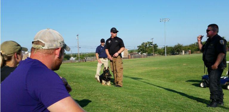 Criminal justice majors watch police officers with a police dog perform a demonstration.